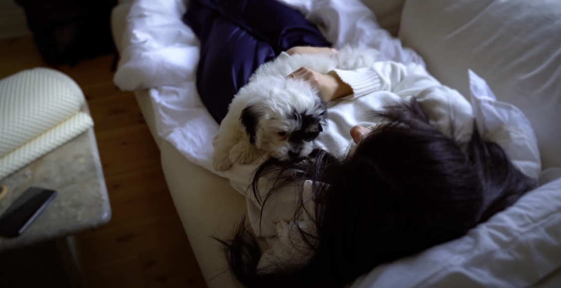 Photo of a girl lying down on the couch, cradling her dog