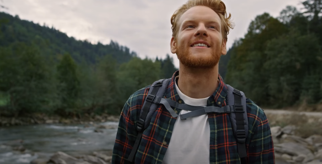 Photo of a guy in a green setting, wearing a checkered polo and smiling