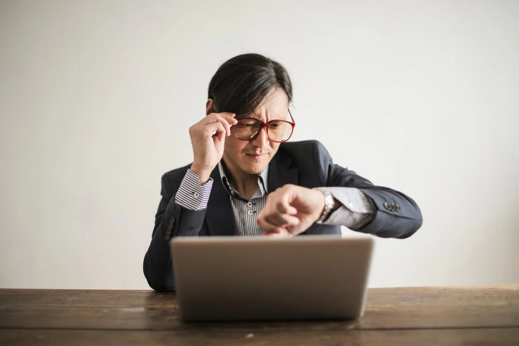 A man who sits at a computer and looks at his watch