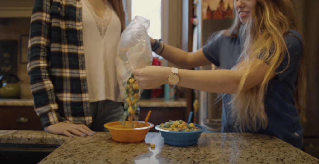 Photo of two friends inside the kitchen, with one friend pouring ingredients into a bowl