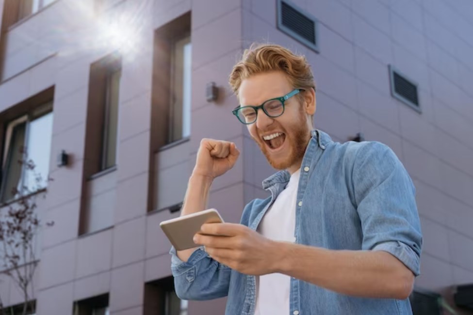 an excited man in glasses looking at his phone's screen and cheering
