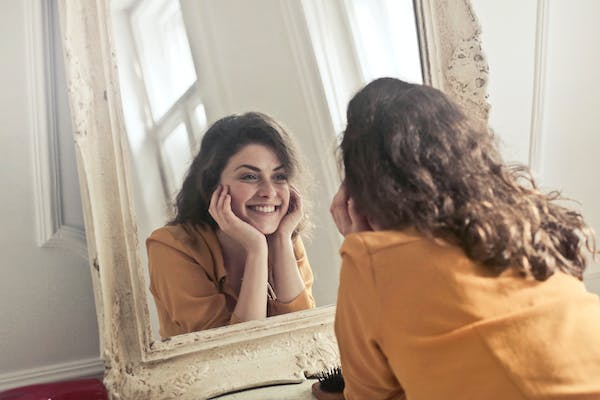 Woman standing in front of a mirror, repeating positive affirmations