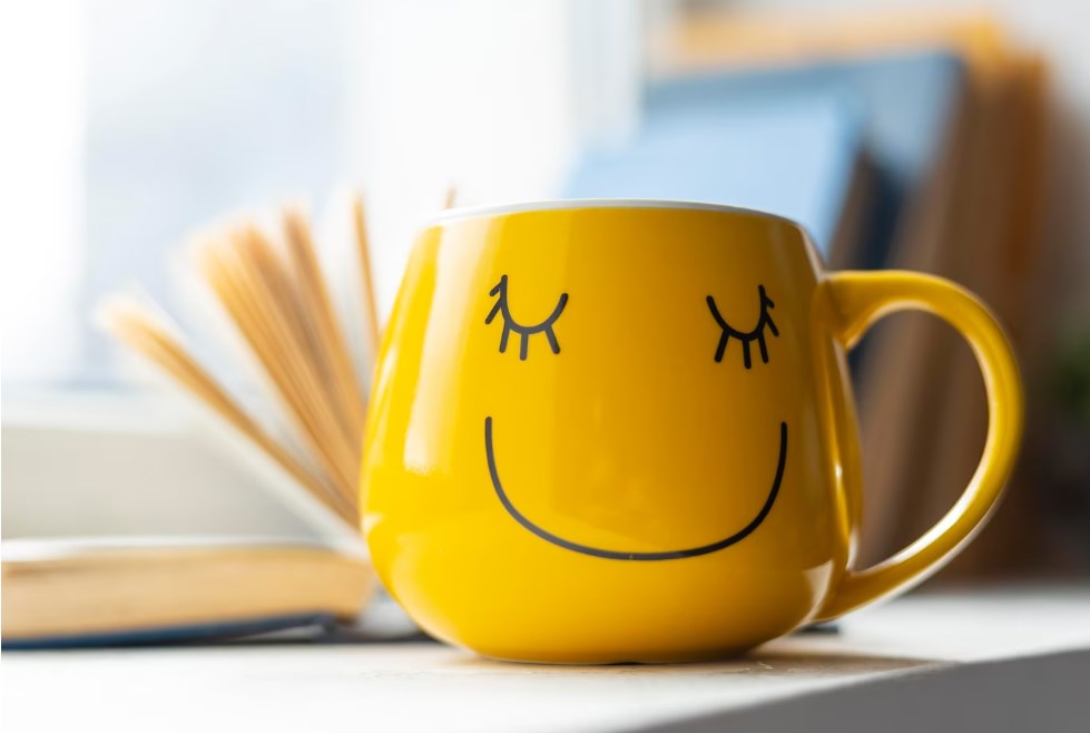 a yellow mug with a smiley face and an open book in the background