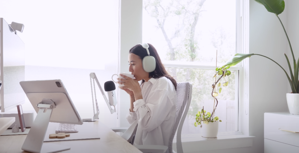 Photo of a girl drinking coffee while wearing a white headset, seated in front of a working table