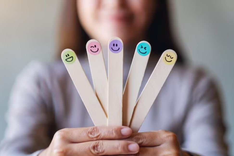 a woman holding colorful hand-drawn happy emotion faces on five wooden sticks