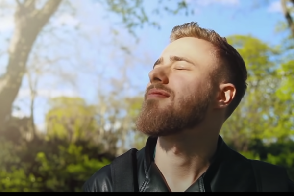 Photo of a relaxed guy closing his eyes outdoors, with a fresh atmosphere surrounding