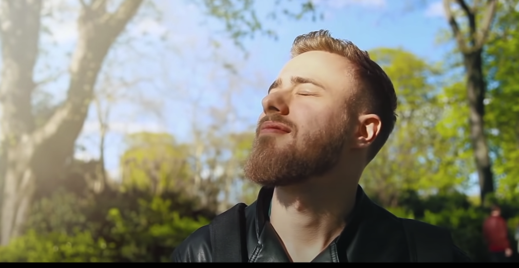 Photo of a relaxed guy closing his eyes outdoors, with a fresh atmosphere surrounding