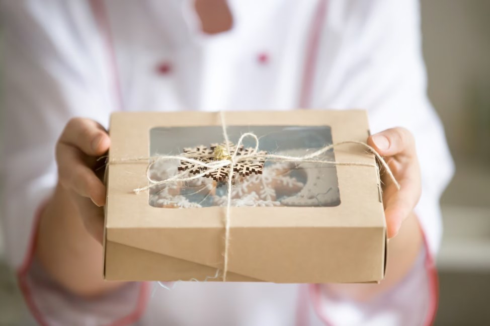 hands of a chef holding out a box with a collection of Christmas cookies