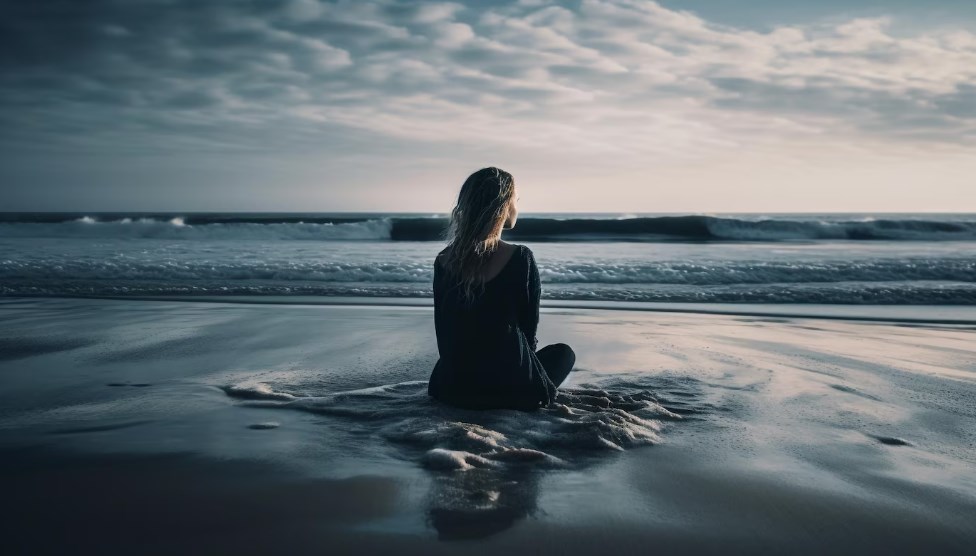 a young woman sitting on the beach in solitude and enjoying a sunset