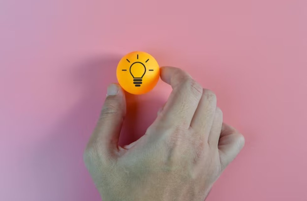 a hand holding an orange plastic ball with a light bulb symbol on it