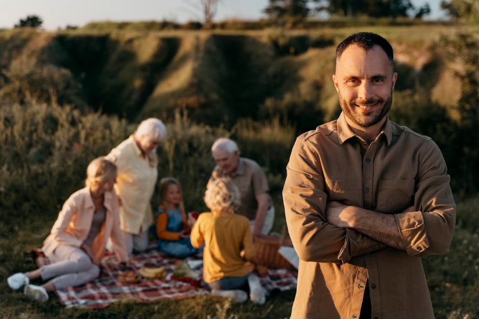 a happy man standing with his arms crossed with his family in the background