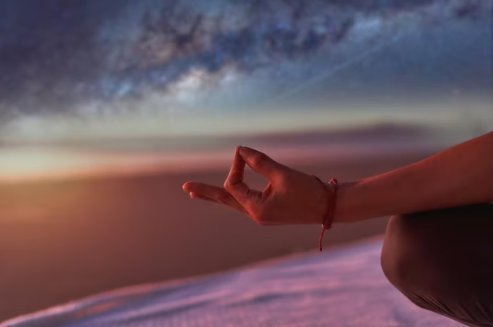 a hand in meditation or yoga practicing outdoors on the beach at sunset
